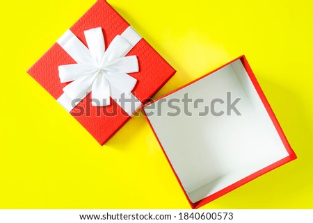 One open and empty red gift box with a lid and a simple white ribbon bow on a yellow background.
