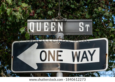 Queen Street sign with a bent one way sign pointing to the left below it