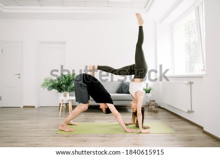 Beautiful sporty fit couple, young man and woman, practicing yoga together at home, doing paired gymnastic yoga asana exercises at home. Balance, meditation and yoga concept