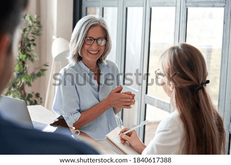 Happy mature old female mentor coach laughing training young interns at group office meeting professional workshop. Cheerful middle aged teacher professor talking to students at university seminar. Royalty-Free Stock Photo #1840617388