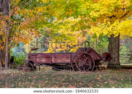 Rusted antique farm machinery sits under a colorful canopy of leaves in this fall still life