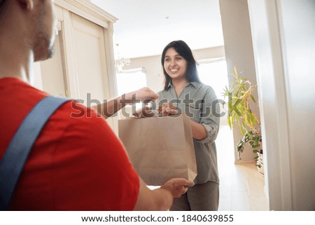 Indian woman customer taking delivery paper eco bag with grocery takeout food meal from man courier holding paper package delivering supermarket or restaurant takeaway order standing at door at home. Royalty-Free Stock Photo #1840639855