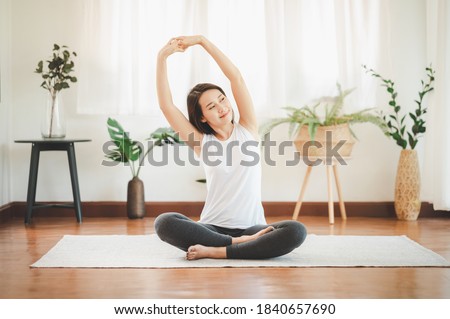 Smiling healthy Asian woman doing yoga shoulder stretching at home in living room Royalty-Free Stock Photo #1840657690