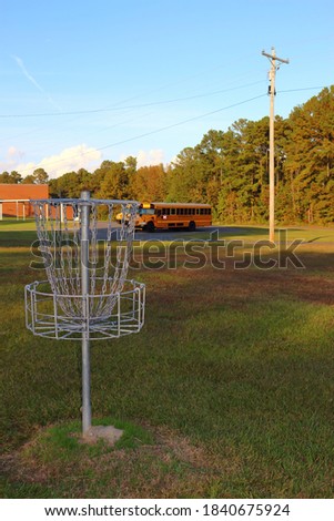 Picture of a disc golf basket with some school buses in the background