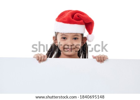Portrait of a happy little girl wearing Santa hat posing behind a white panel isolated on white background holding a blank board Christmas billboard