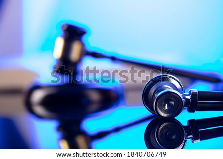 Medical law concept. Judges gavel, stethoscope, open book. Blue light, table and background.