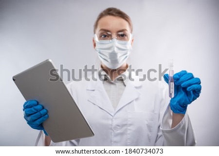 Female microbiologist in biohazard protective clothing explore biological tube with vaccine and using laptop. White background. Research and development concept.