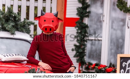 A young man in a bull ox costume is a symbol of the new year against the background of a red car, a festive Christmas tree, decorated with garlands of porch lights with a wreath. Copy space, template