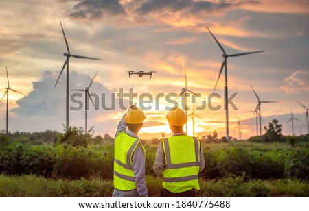 two asian engineers male flying drone surveying and checking wind turbines from the high angle view of the field during beautiful sunset. using drone technology for work. Alternative energy for future Royalty-Free Stock Photo #1840775488