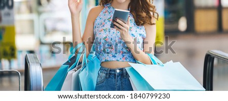 Lifestyle shopping concept, Young happy asian woman using mobile phone with paper bag in shopping mall, Bangkok, Thailand
