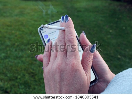 A woman's hand holds a cigarette against the background of a phone in the Park, side view-the concept of acquired bad habits
