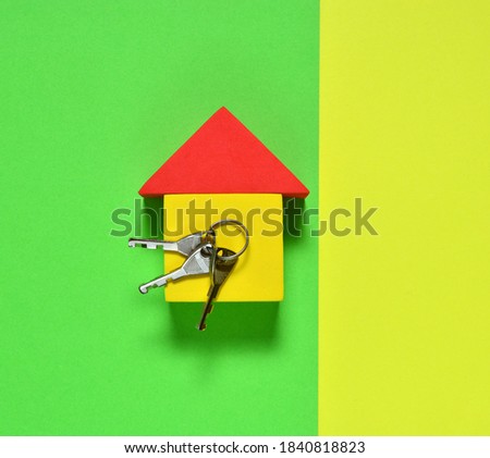 keys and a toy house with a red roof on a green and yellow background. concept of mortgage, home loan, own new house and apartment. flat lay.