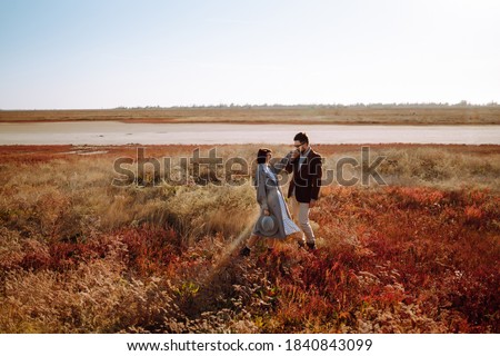 Young loving couple walking and hugging in autumn field. Enjoying time together. Fashion, lifestyle and autumn mood.
