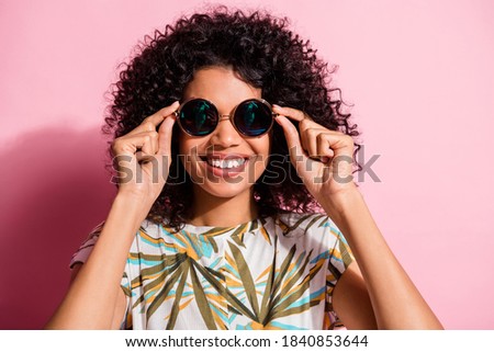Portrait photo of black skinned curly woman wearing round stylish sunglass smiling isolated on pastel pink color background