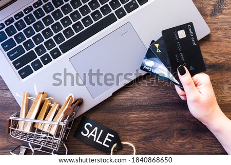 Female hands are holding credit cards for online shopping. Woman is ready to buy clothes, products, technics by laptop computer. Black friday concept. Discount seasonal sale. Cashless payment.