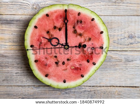 Watermelon slice with arrows showing ten o'clock, light wooden background. Horizontal orientation