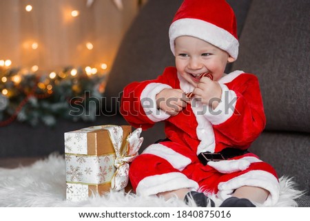 A beautiful little boy in a Santa Claus costume with a Lollipop in his hands on the background of Christmas lights. The concept of Christmas celebration. New year holiday.