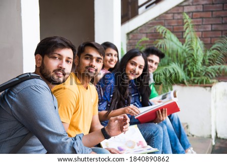Young Asian Indian college students reading books, studying on laptop, preparing for exam or working on group project while sitting on grass, staircase or steps of college campus Royalty-Free Stock Photo #1840890862