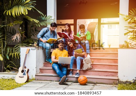 Young Asian Indian college students reading books, studying on laptop, preparing for exam or working on group project while sitting on grass, staircase or steps of college campus Royalty-Free Stock Photo #1840893457