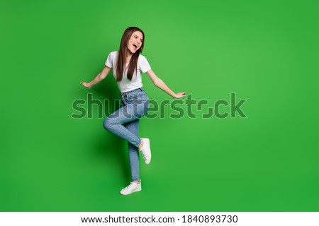 Full length photo of adorable dreamy young lady dancing wear jeans t-shirt footwear isolated on green background
