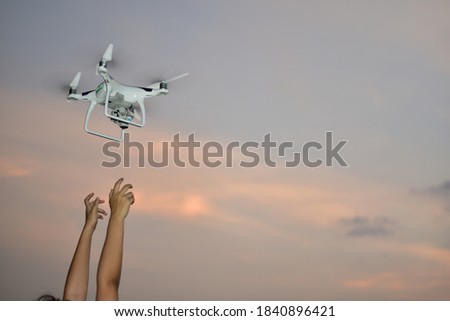 drone flying front of orange sky evening day for take aerial photo landscape by gimbal camera have 2 women hands for receiving landing.