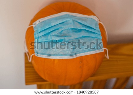 Photo of an orange Halloween pumpkin with a disposable face mask. 