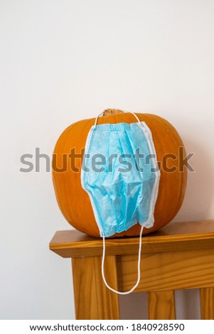 Photo of an orange Halloween pumpkin with a disposable face mask. 