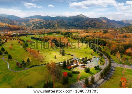 Aerial panorama of fall colors on the green grassy meadows in Hoshino Resorts Tomamu and beautiful mountains in the background on a sunny cloudy autumn day, in Shimukappu Village, Hokkaido, Japan