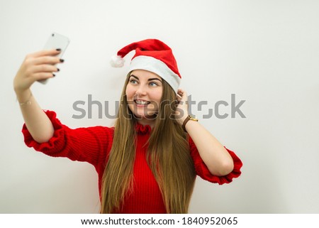 girl takes a selfie photo on her phone, wearing a Santa Claus hat, white blank background for text, happy new year and Christmas online
