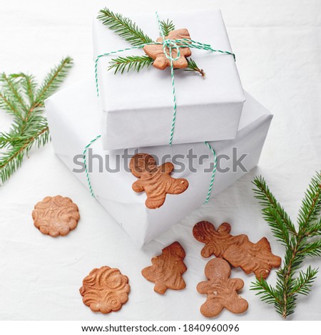 Christmas gifts wrapped in white paper and decorated with spruce sprigs and gingerbread cookies on a fabric background