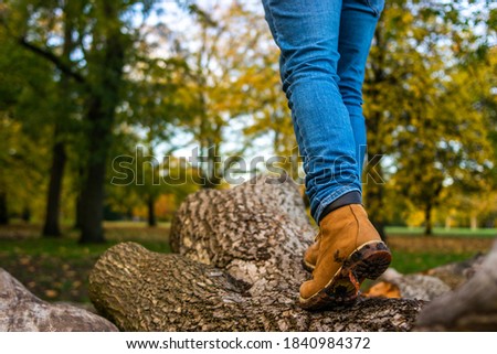 Photo of the legs on a young man wearing mountain boots and jeans walking in a tree trunk during an autumn day in the park