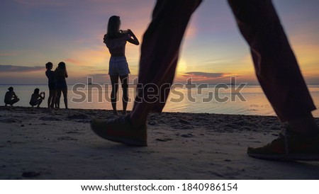 Silhouettes of people on the sandy beach enjoying the sunset and taking pictures on smartphones against the background of the sea