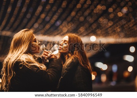 Caucasian young girls with champagne and lights on the street, cheerful company of girls and celebration, new year and christmas