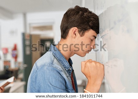 Disappointed university student leaning on whiteboard with closed eyes. Tired high school guy feeling failure in classroom. Side view of sad young college student trying to solve math problem. Royalty-Free Stock Photo #1841011744