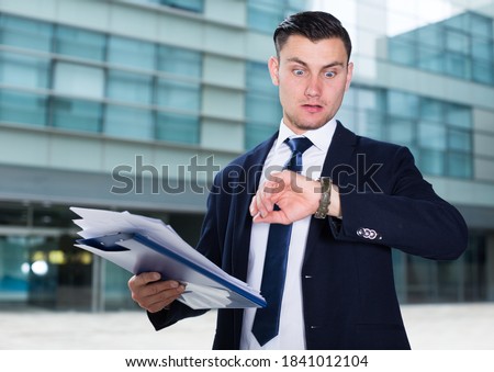 Businessman in suit is looking on watch near the office and understand that he late. Royalty-Free Stock Photo #1841012104