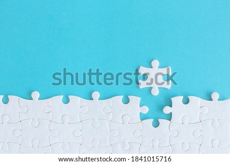 Assembling jigsaw puzzle pieces, Top view unfinished white jigsaw puzzle on blue background, Fragment of a folded white jigsaw puzzle with copy space, Teamwork and problem solving concept.  Royalty-Free Stock Photo #1841015716