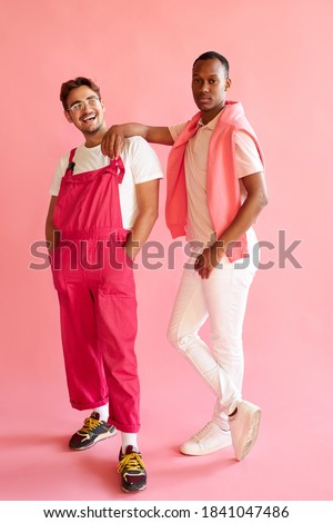 positive caucasian and afro american men in stylish wear posing at camera in studio, thye smile, male models in bright fashionable clothes, people diversity concept