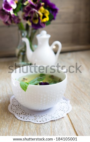 Glasses of green mint tea and vase with fresh violas on the table