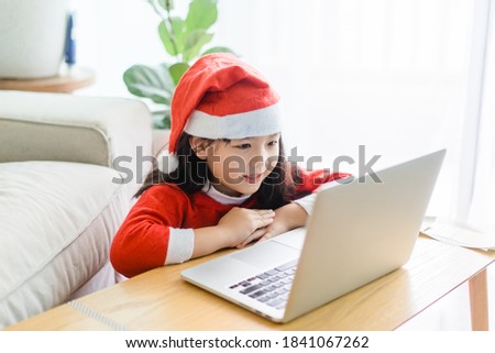 Asian girl with santa hat on christmas holidays party.Happy girl talking video cameara on laptop.Technology online with laptop at home.New normal.Covid-19 coronavirus.Social distancing.stay home.