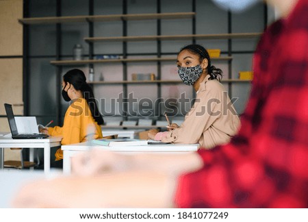 Young students with face masks at desks at college or university, coronavirus concept.