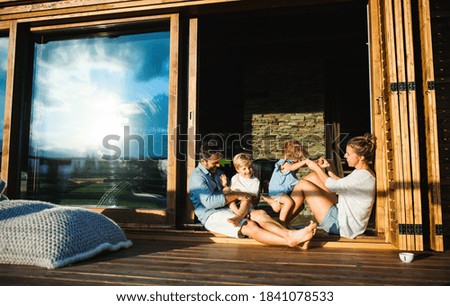 Family with small children sitting on patio of wooden cabin, holiday in nature concept.