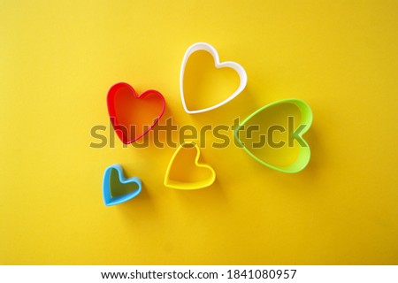 Plastic molds of multi colors for making cookies in the shape of a hearts on a yellow background. Culinary or party concept. Flat lay.