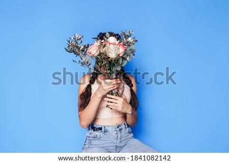 Young woman sitting on a small stepladder and holding a beautiful bouquet of white roses in her hands on blue background spring time.