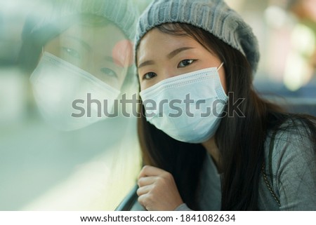 lifestyle portrait of young attractive and pretty Asian woman wearing mask in railcar traveling in new normal virus time - sweet Japanese girl by train window smiling cheerful