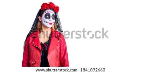 Woman wearing day of the dead costume over background smiling looking to the side and staring away thinking. 