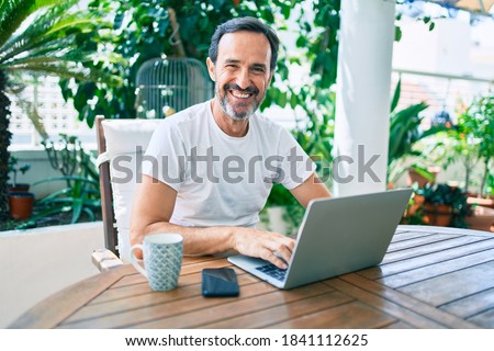 Middle age man with beard smiling happy at the terrace working from home using laptop Royalty-Free Stock Photo #1841112625
