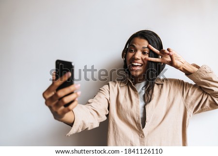 Happy african american woman gesturing peace sign while taking selfie on cellphone isolated over white background