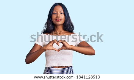 Young indian girl wearing casual clothes smiling in love showing heart symbol and shape with hands. romantic concept. 