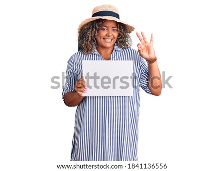 Young african american plus size woman holding cardboard banner with blank space doing ok sign with fingers, smiling friendly gesturing excellent symbol 