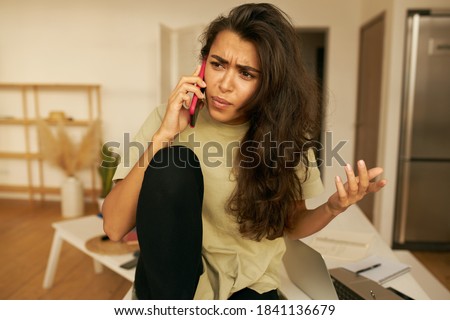 Frustrated young Hispanic woman being angry because of spam unwanted robocall. Dissatisfied annoyed female customer complaining about internet service on mobile phone, expressing indignation